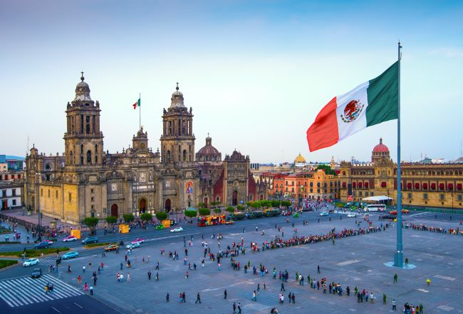 The Zócalo in Mexico City, showcasing the Mexican flag and National Palace on a sunny day.